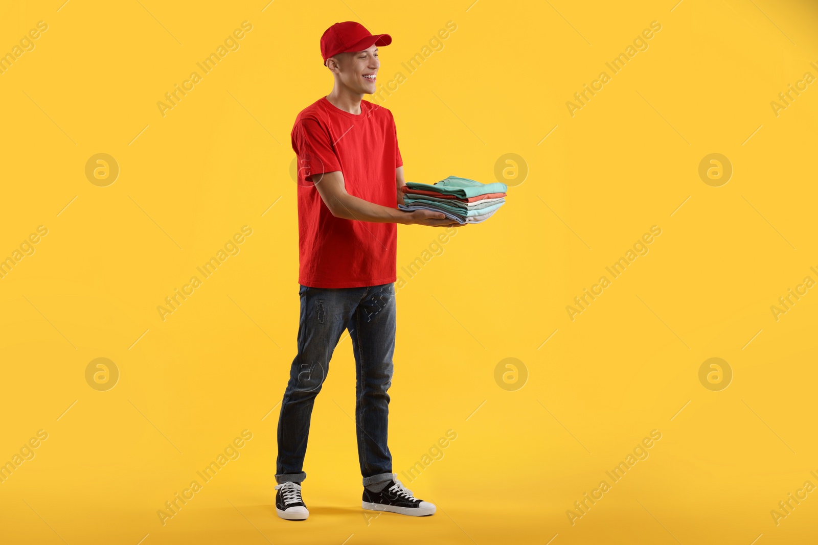 Photo of Dry-cleaning delivery. Happy courier holding folded clothes on orange background
