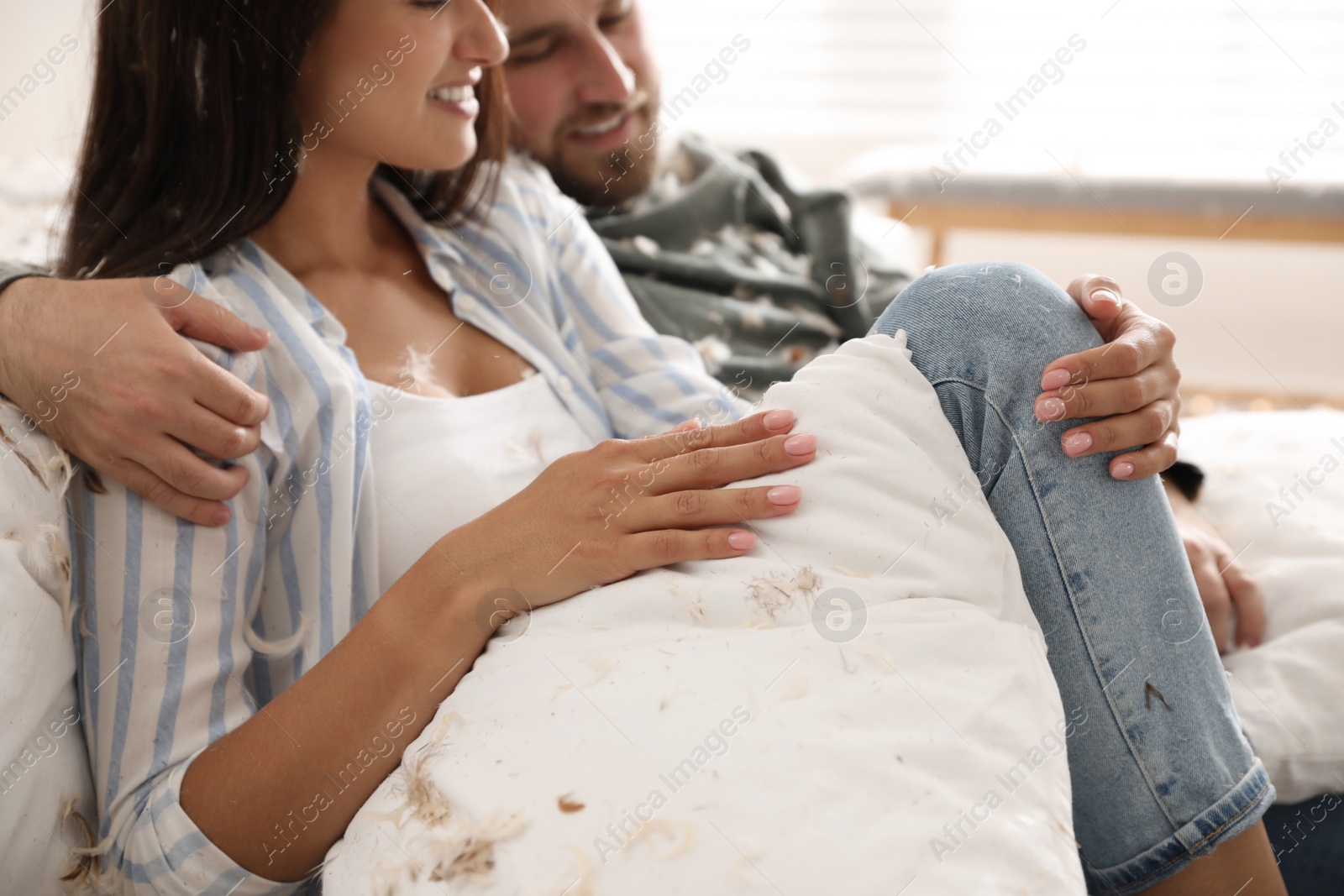 Photo of Happy young couple resting after fun pillow fight at home, closeup