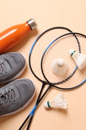 Photo of Feather badminton shuttlecocks, sneakers and bottle on beige background, flat lay