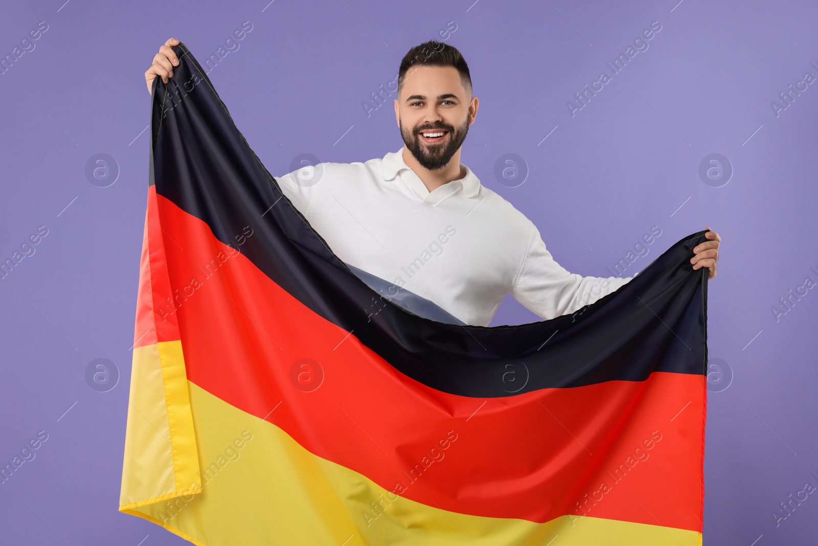 Photo of Young man holding flag of Germany on purple background