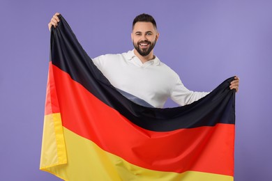 Young man holding flag of Germany on purple background
