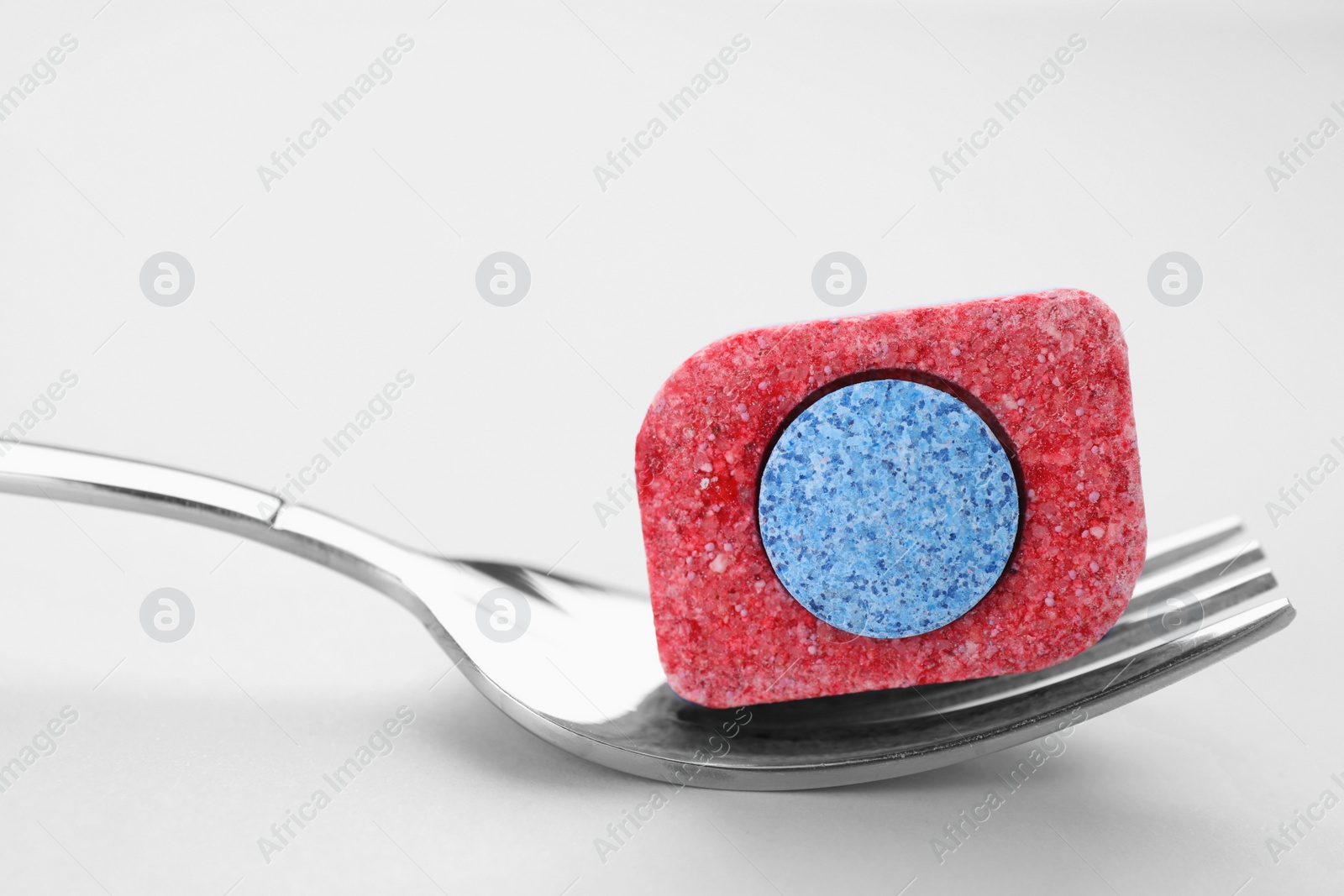 Photo of Fork with dishwasher detergent tablet on light background, closeup