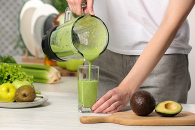 Photo of Woman pouring tasty green smoothie into glass at white wooden table, closeup