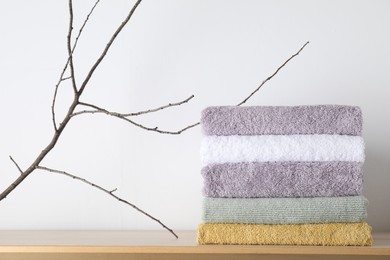 Stacked terry towels and tree branch on wooden table near white wall