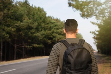 Man with backpack on road near forest, back view