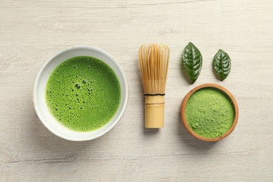 Cup of fresh matcha tea, green powder and bamboo whisk on white wooden table, flat lay