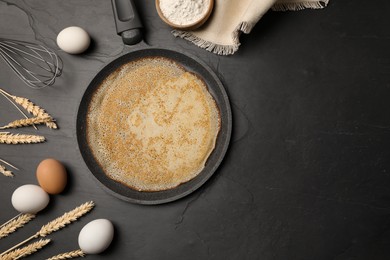 Frying pan with delicious crepe, spikelets and ingredients on black table, flat lay. Space for text