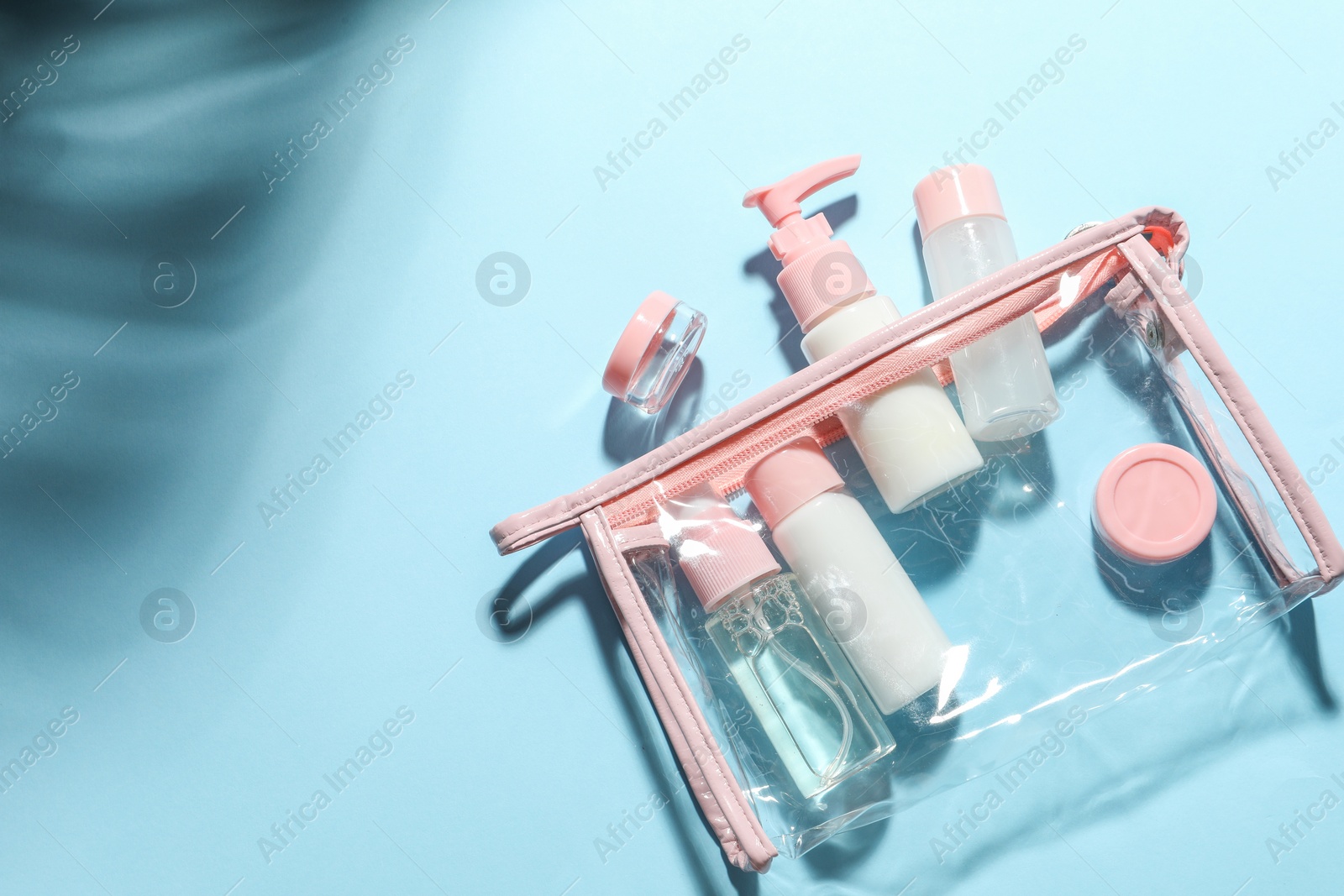 Photo of Cosmetic travel kit with plastic bag on light blue background, top view. Space for text