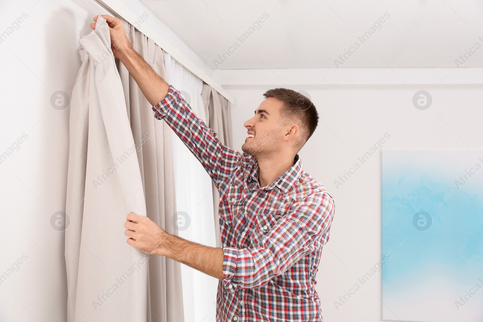 Photo of Man hanging window curtain indoors. Interior decor element