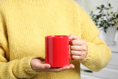 Photo of Woman holding red mug at home, closeup. Mockup for design