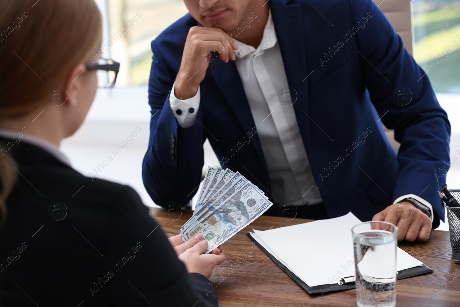 Photo of Woman offering bribe money to man at table, closeup