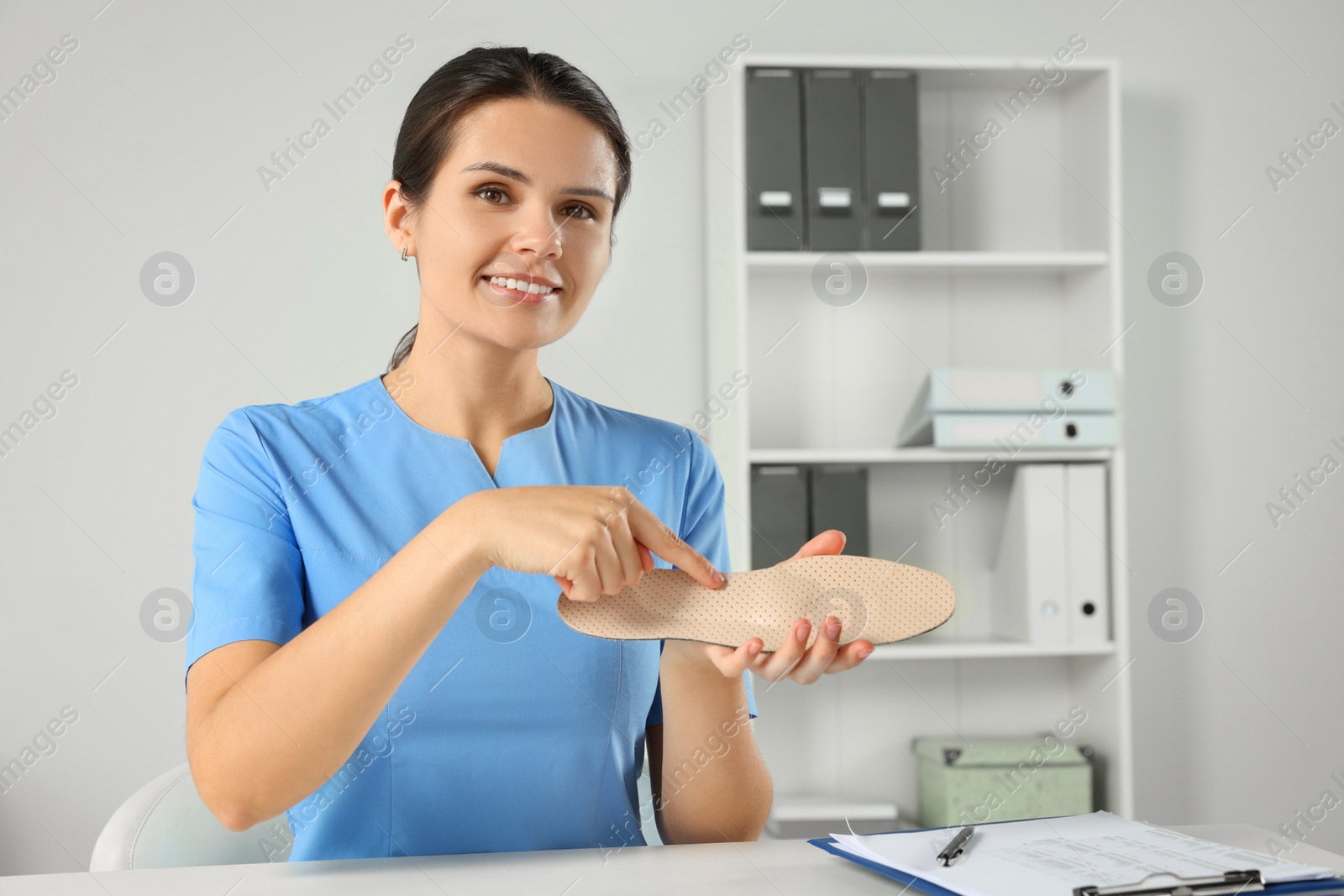 Photo of Beautiful female orthopedist showing insole at table in hospital