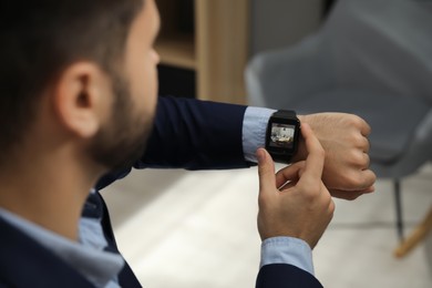 Businessman checking home security system via smartwatch app in office, closeup. Image of room through CCTV camera on display