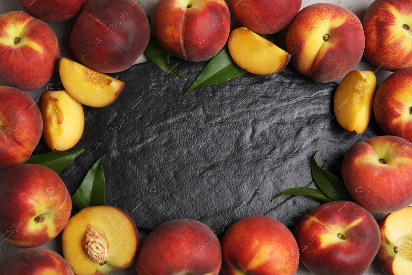 Photo of Frame made of fresh peaches and leaves on slate plate, flat lay with space for text