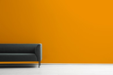 Photo of Stylish grey sofa near orange wall indoors, space for text. Interior design