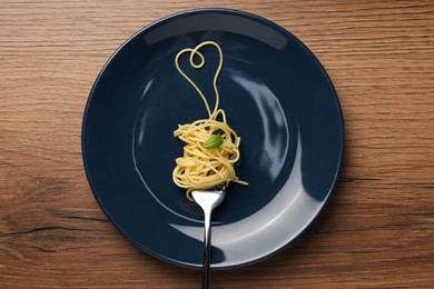 Heart made with spaghetti and fork on wooden table, top view