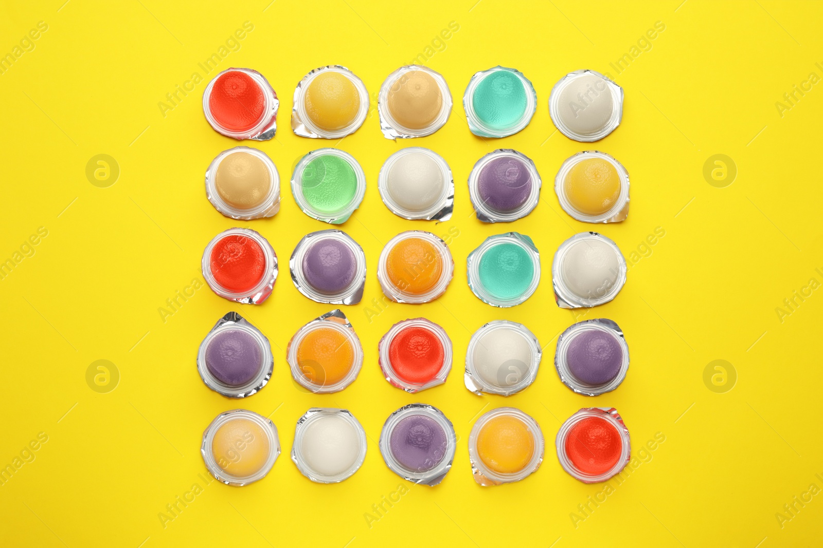 Photo of Tasty bright jelly cups on yellow background, flat lay