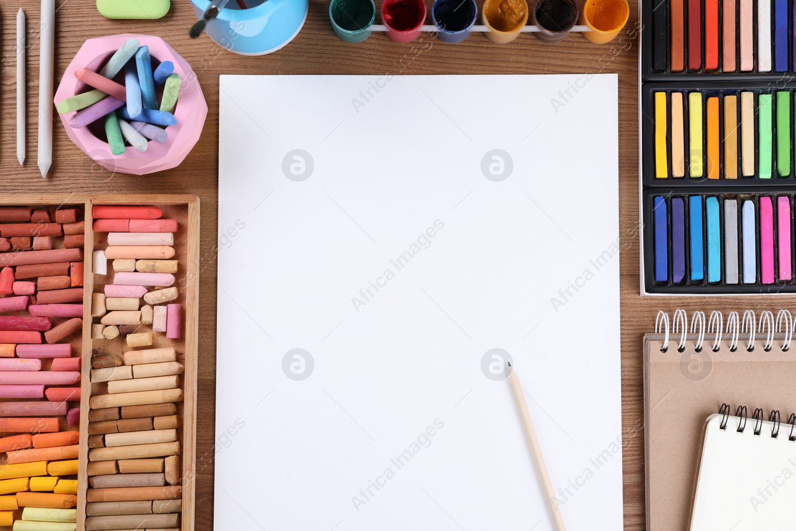 Photo of Blank sheet of paper, colorful chalk pastels and other drawing tools on wooden table, flat lay. Modern artist's workplace