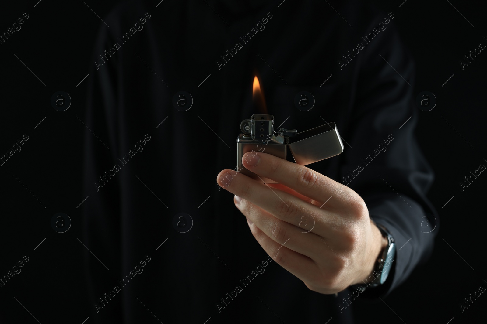 Photo of Man holding lighter with burning flame on black background, closeup. Space for text