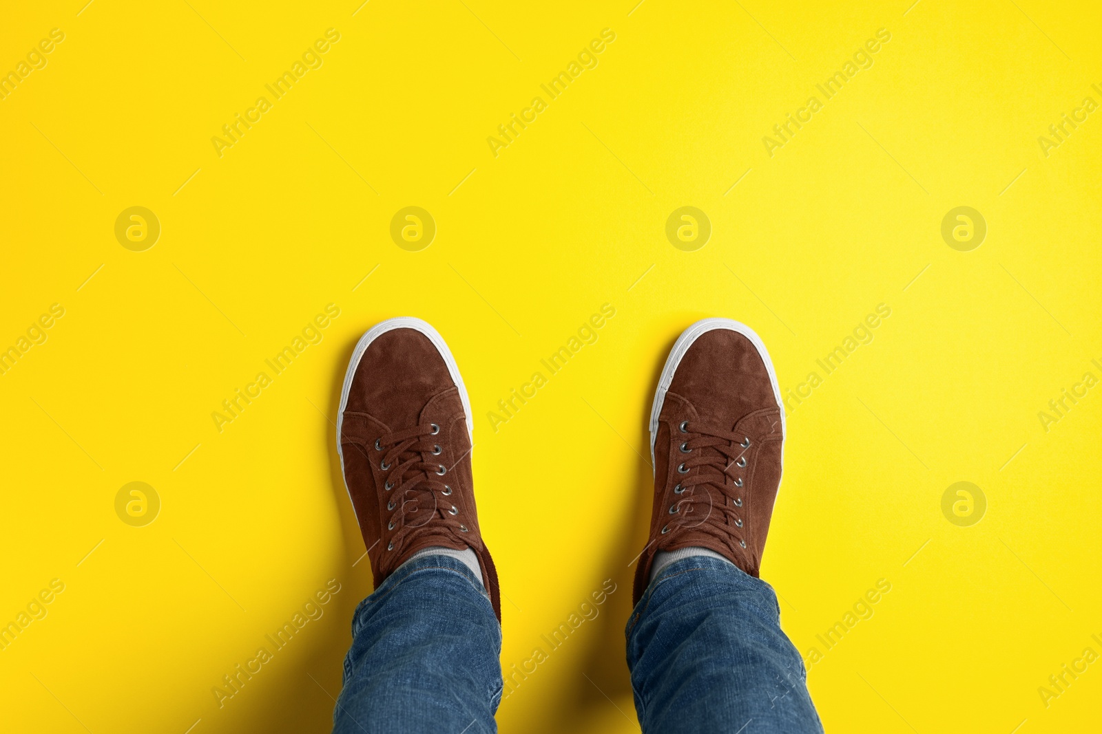 Photo of Man in stylish sneakers standing on yellow background, top view