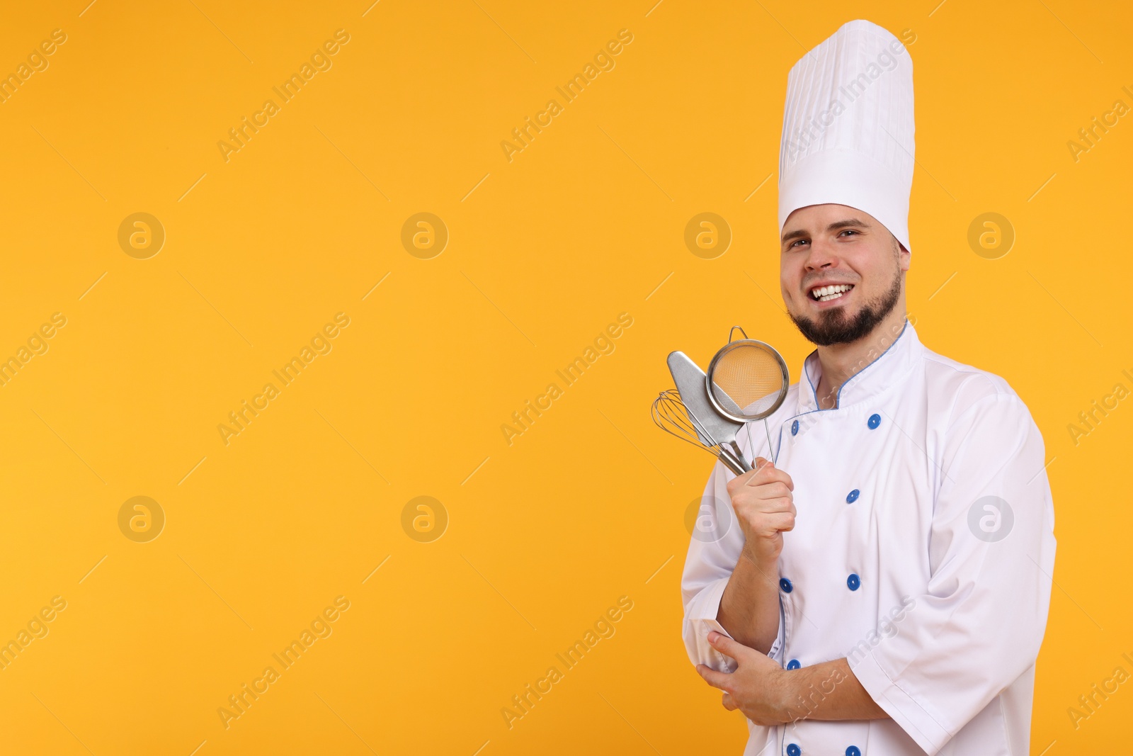 Photo of Happy confectioner in uniform holding professional tools on yellow background. Space for text