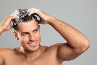 Handsome man washing hair on grey background