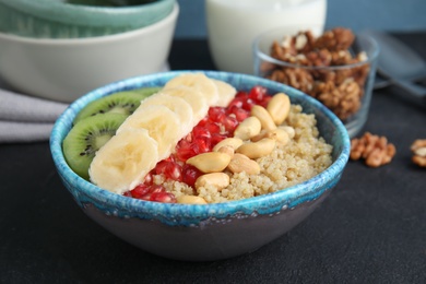 Bowl of quinoa porridge with peanuts, kiwi, banana and pomegranate seeds on black table