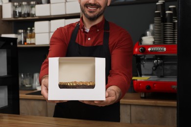 Photo of Business owner in his cafe. Man holding box with cake at desk, selective focus