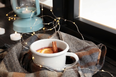 Photo of Composition with cup of hot winter drink, scarf and Christmas lights near window. Cozy season