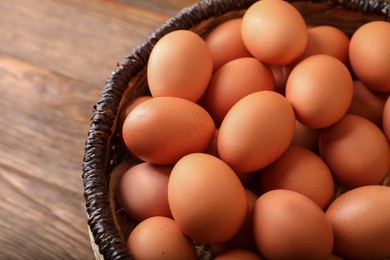 Photo of Raw chicken eggs in wicker basket on wooden table, closeup