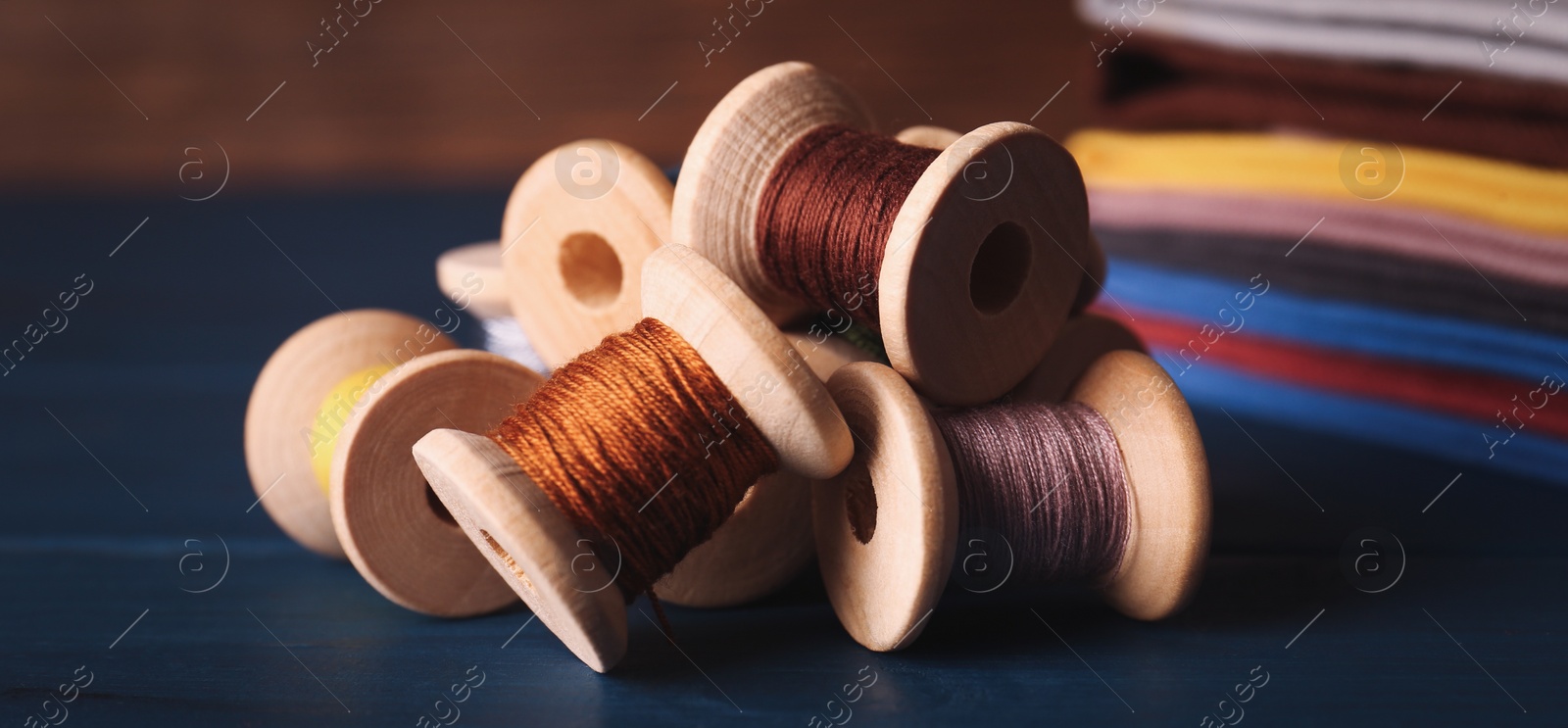 Photo of Set of color sewing threads on blue wooden table, closeup