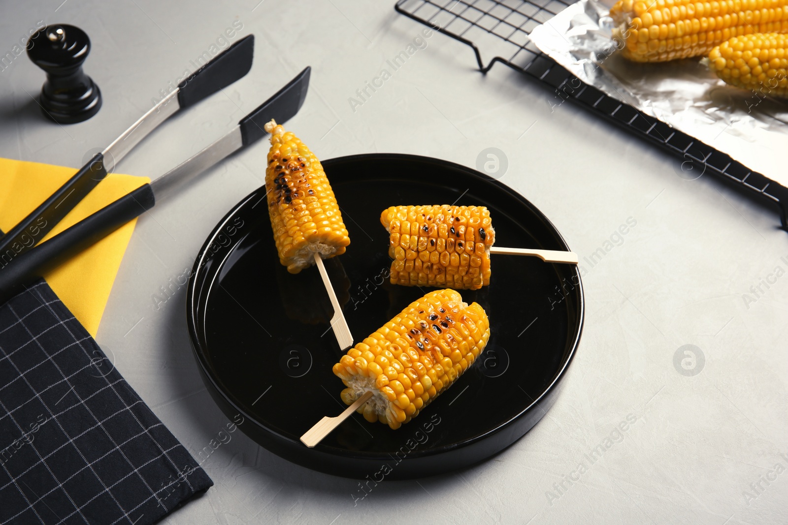 Photo of Ceramic plate with grilled corn cobs on light background