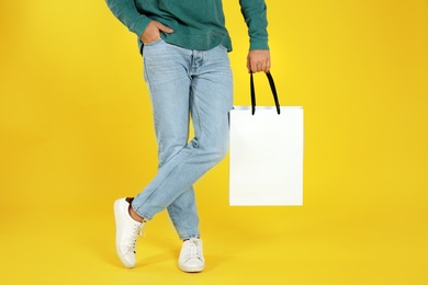 Young man holding paper bag on color background, closeup.  Mockup for design