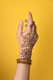 Woman with beautiful henna tattoo on hand against yellow background, closeup. Traditional mehndi