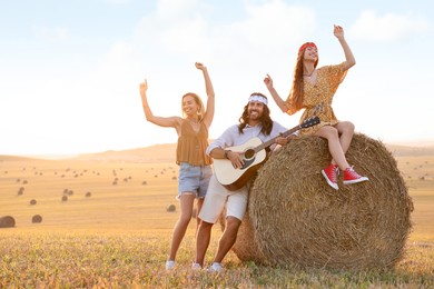 Photo of Beautiful hippie women listening to their friend playing guitar in field, space for text