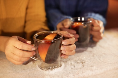 Friends with cups of mulled wine at snowy table, closeup