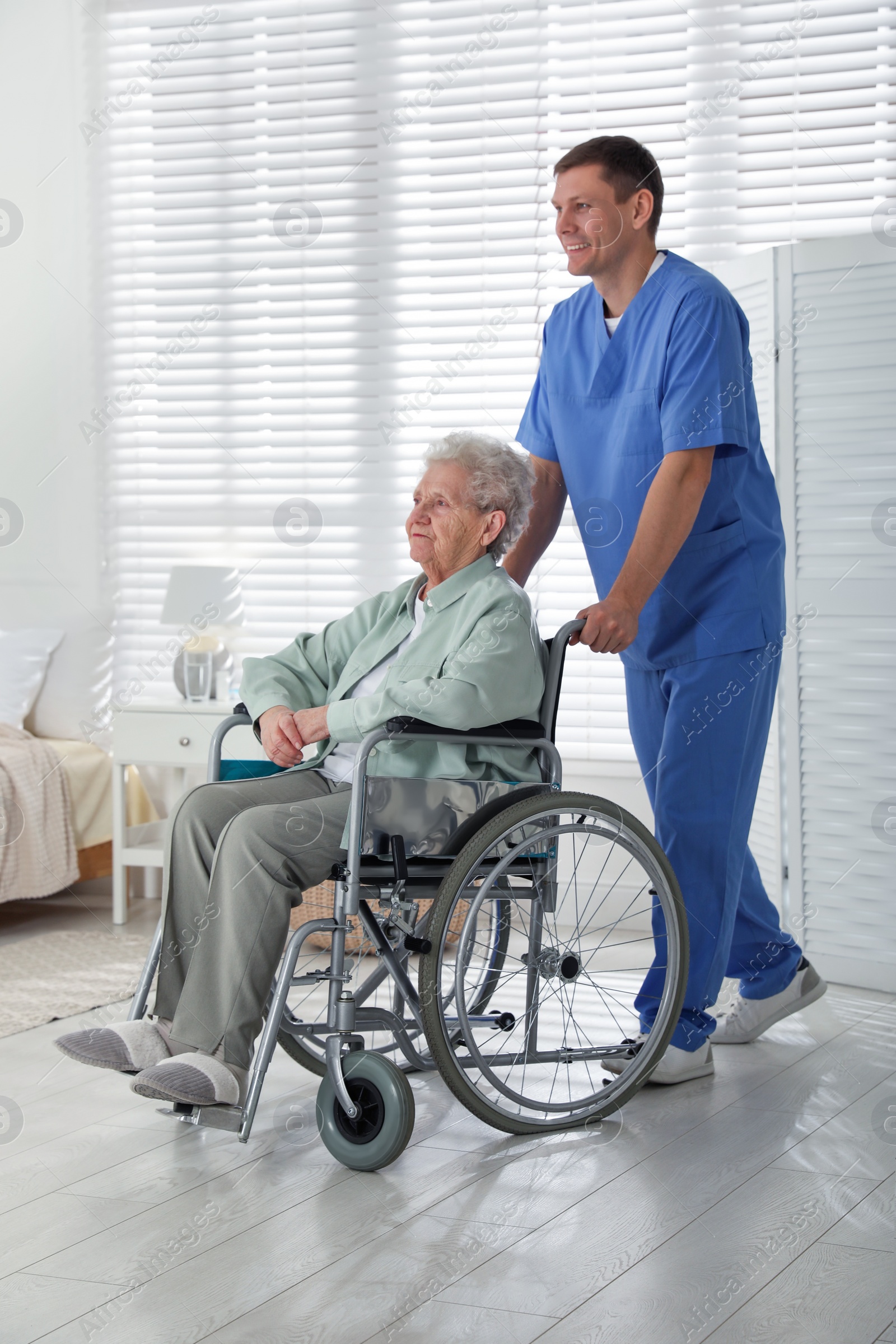 Photo of Caregiver assisting senior woman in wheelchair indoors. Home health care service