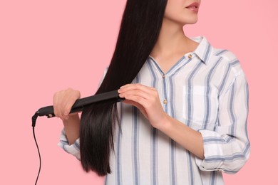 Photo of Woman using hair iron on pink background, closeup