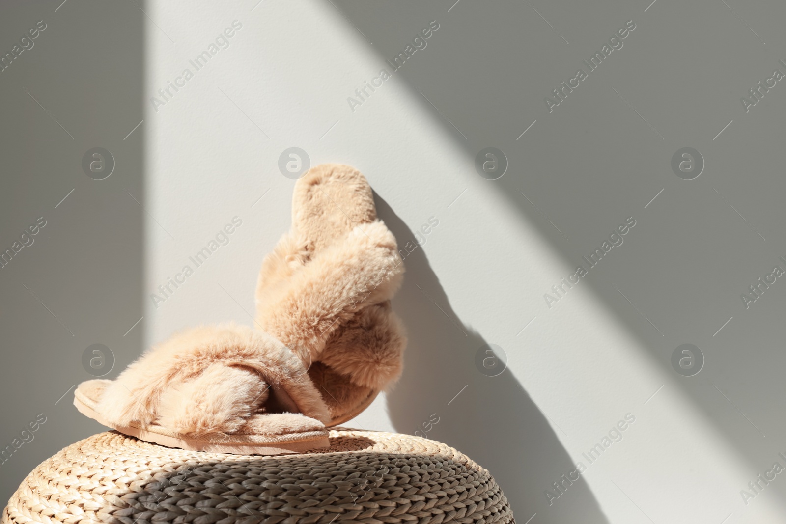 Photo of Pair of soft slippers on wicker pouf near white wall, space for text