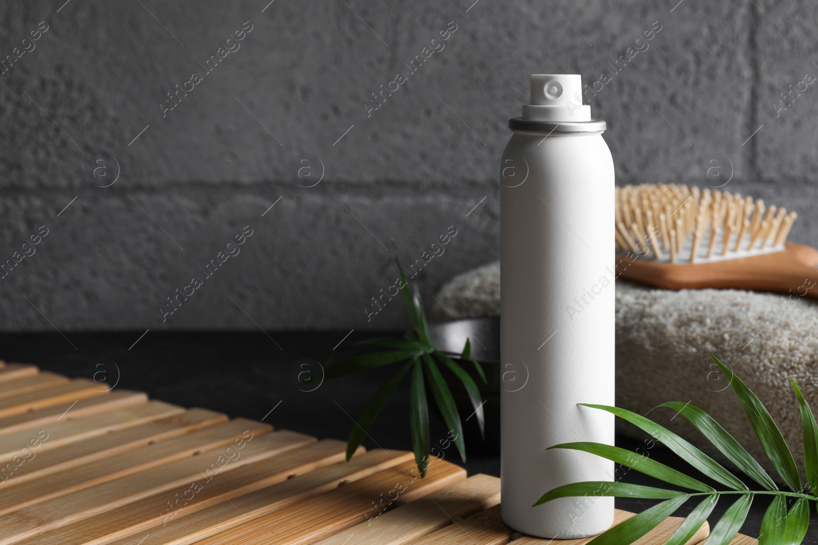 Photo of Dry shampoo spray, hairbrush and towel on wooden table near grey wall. Space for text