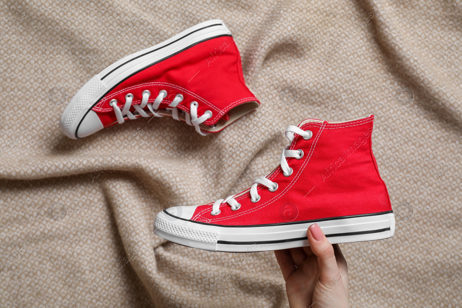 Photo of Woman holding new stylish red sneaker on beige cloth, top view