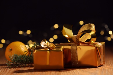 Photo of Golden gift boxes and tangerine on wooden table against blurred lights, space for text