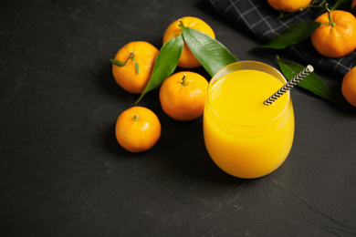 Photo of Glass of fresh tangerine juice and fruits on black table