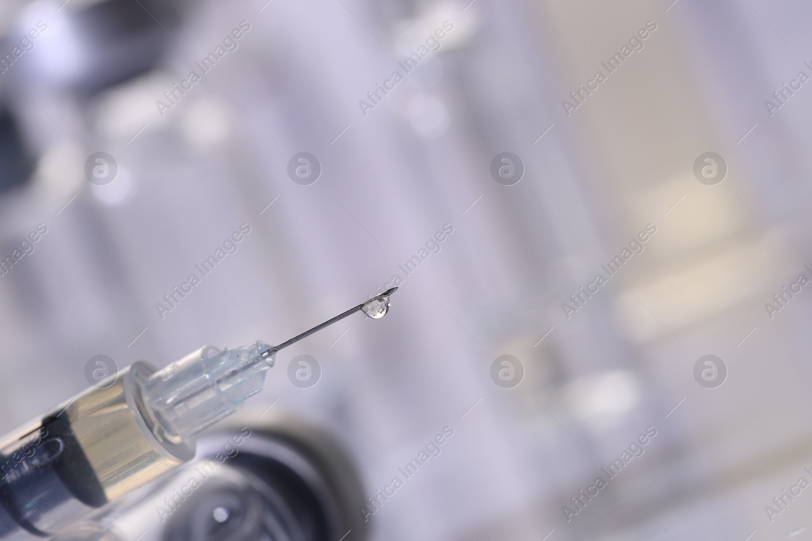 Photo of Drop of medication on syringe needle against blurred background, closeup. Space for text