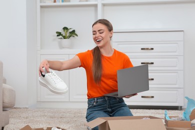 Photo of Happy woman with laptop unpacking parcels at home. Online store