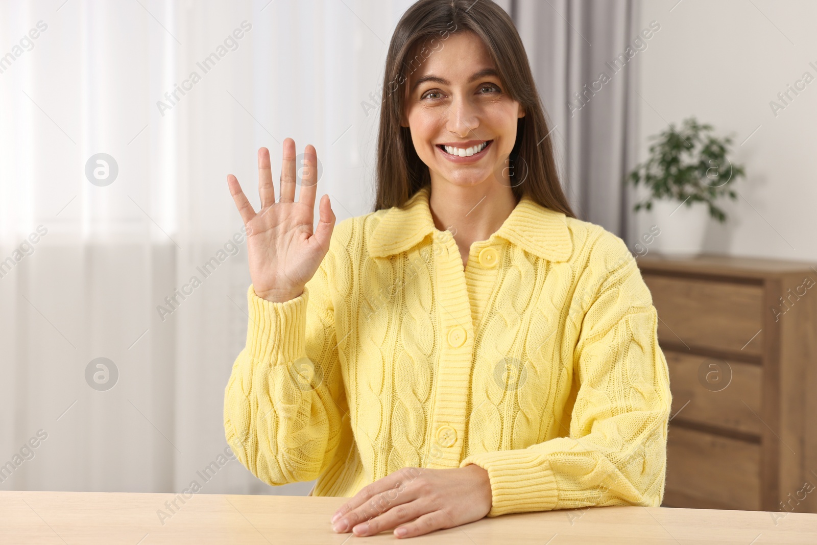 Photo of Happy woman waving hello at table indoors