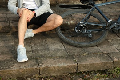 Photo of Man with injured knee on steps near bicycle outdoors, closeup