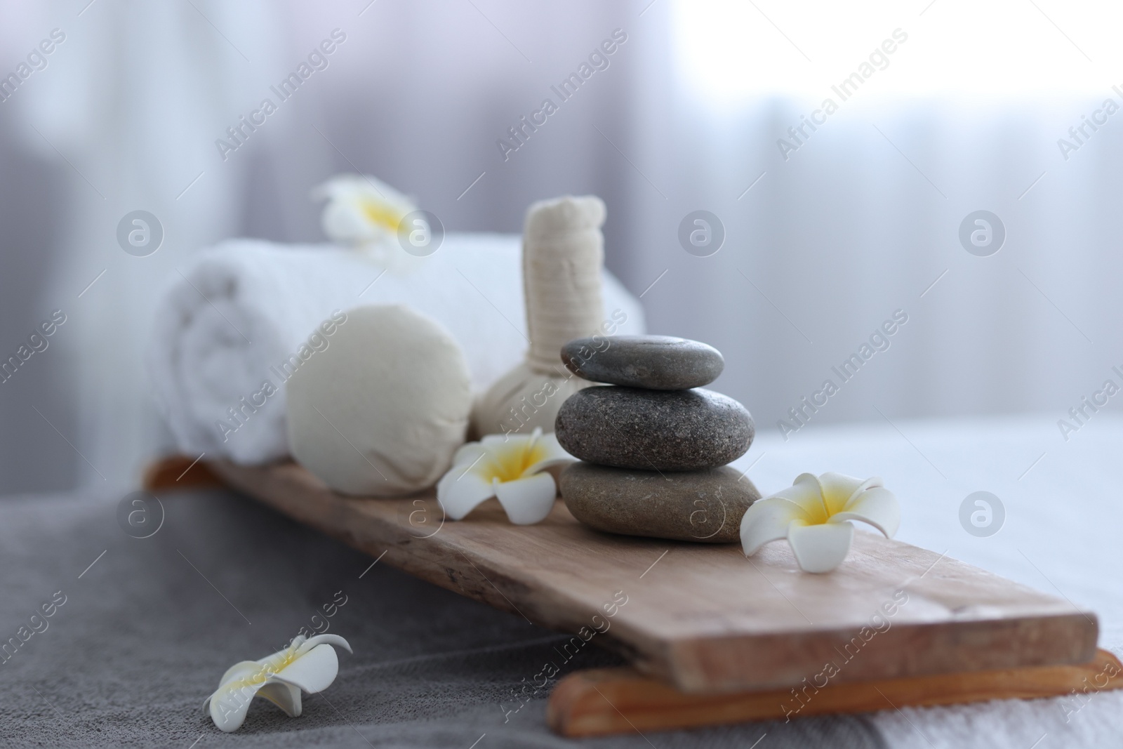 Photo of Stacked spa stones, flowers, herbal bags and towel on massage table indoors