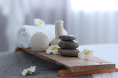 Photo of Stacked spa stones, flowers, herbal bags and towel on massage table indoors