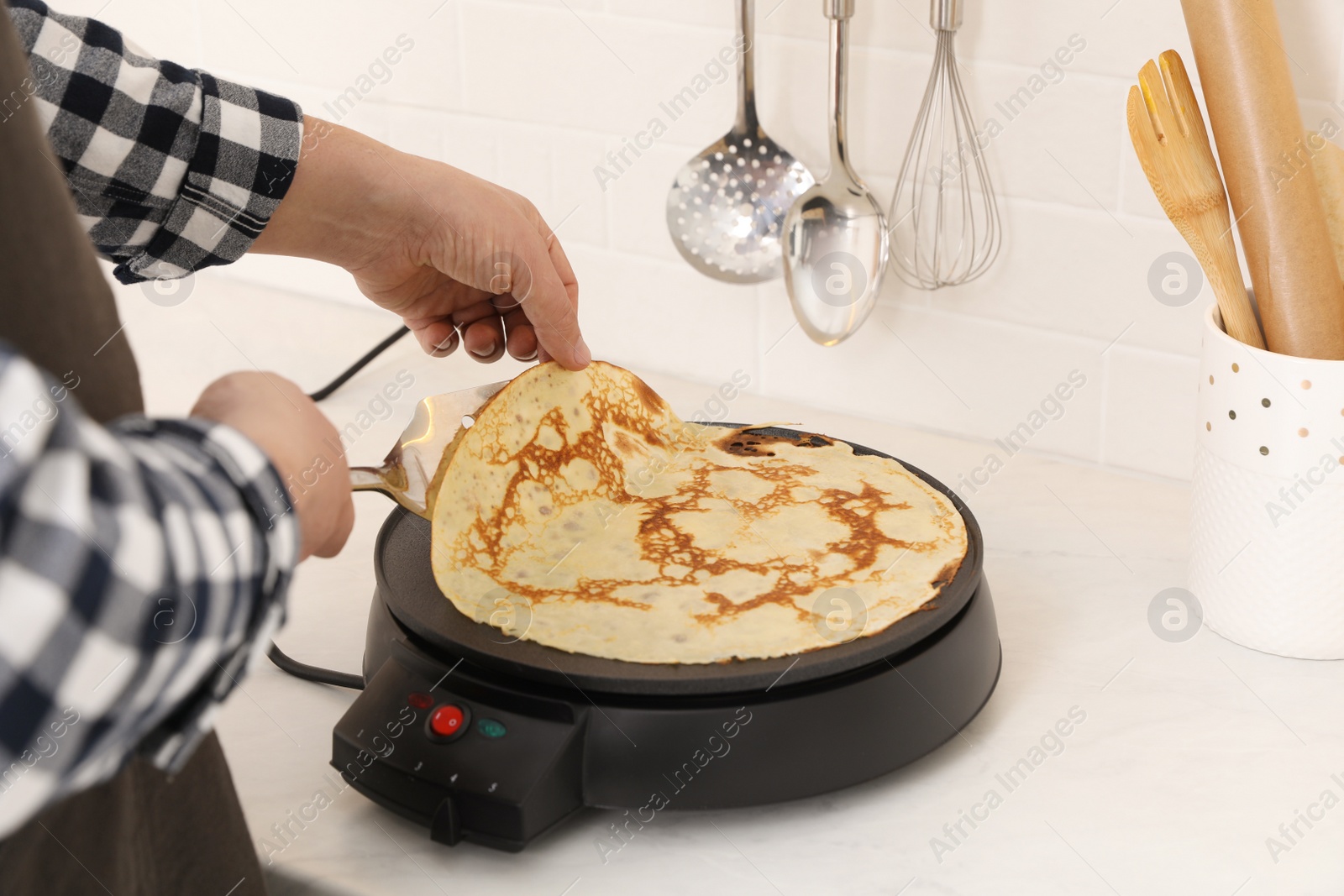 Photo of Man cooking delicious crepe on electric pancake maker in kitchen, closeup